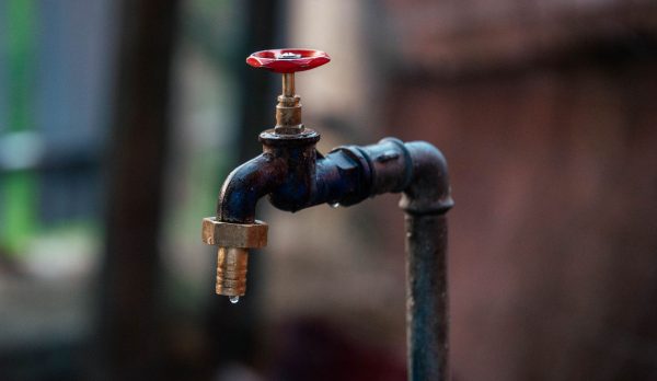 A rusty outdoor tap with a single drop of water