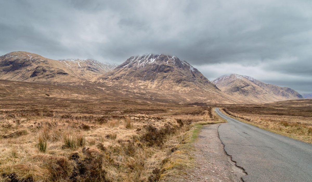 Road leading through remote Scottish Highlands with majestic mountains under cloudy skies
