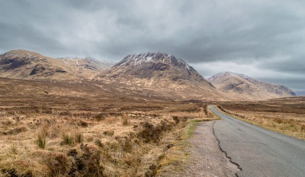 Road leading through remote Scottish Highlands with majestic mountains under cloudy skies