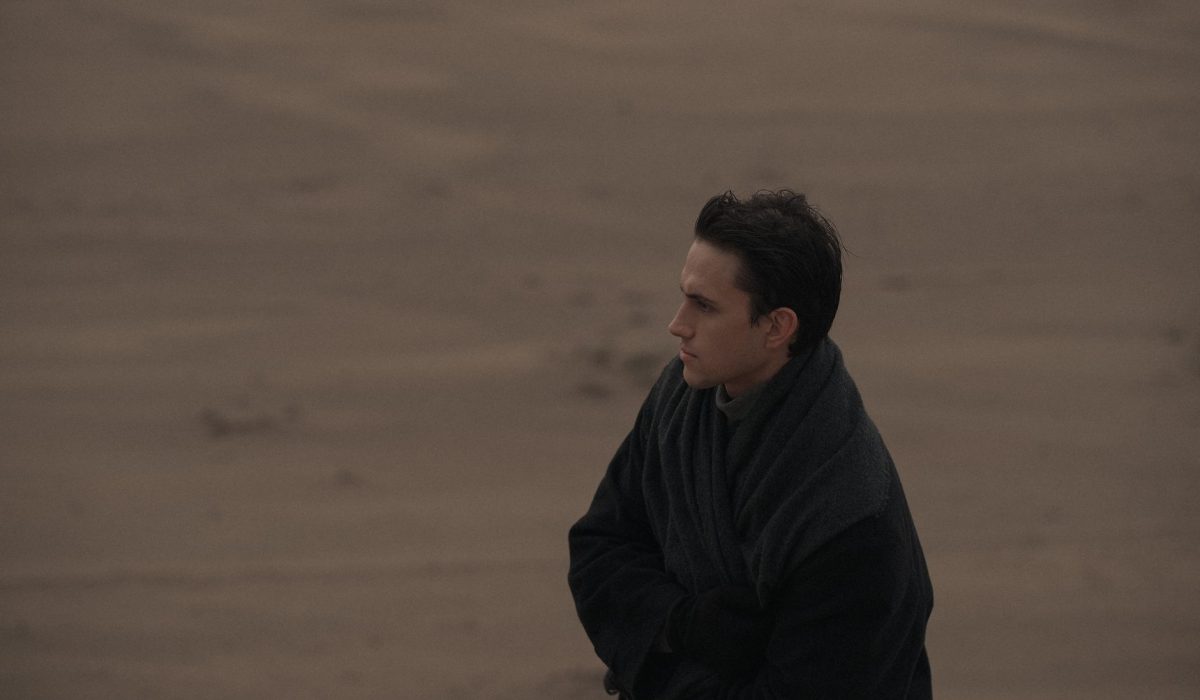 A man standing alone on a deserted beach, wrapped in a dark coat