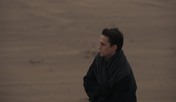 A man standing alone on a deserted beach, wrapped in a dark coat