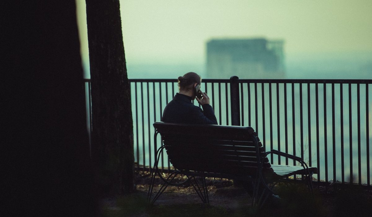 Silhouette of a man on a park bench overlooking a hazy cityscape