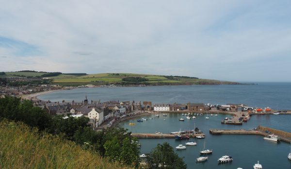 A picturesque view of Stonehaven harbor with moored boats and coastal townscape under a cl
