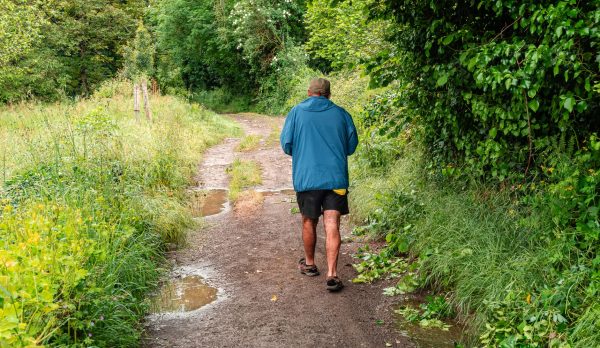 A man walks a muddy path between hedges