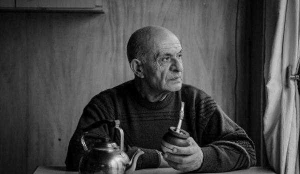Elderly man holding a cup, gazing out a window