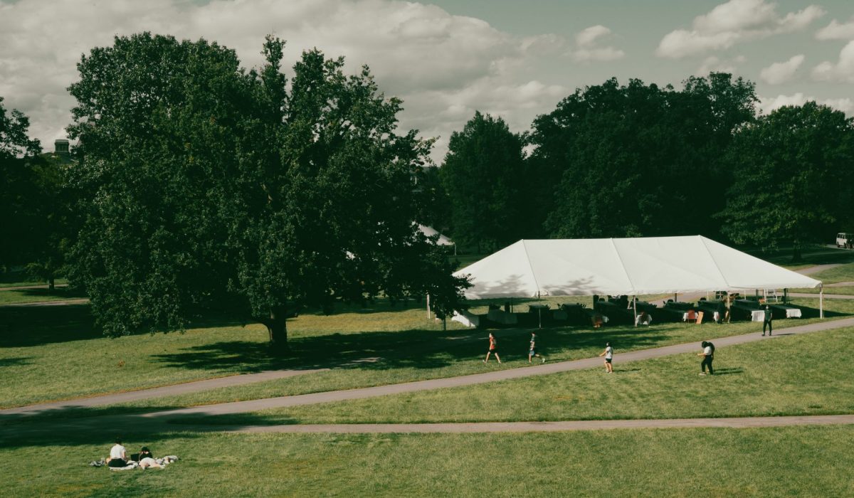 Aerial photo of a park with a large white tent, people enjoying greenery and blue skies