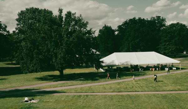 Aerial photo of a park with a large white tent, people enjoying greenery and blue skies